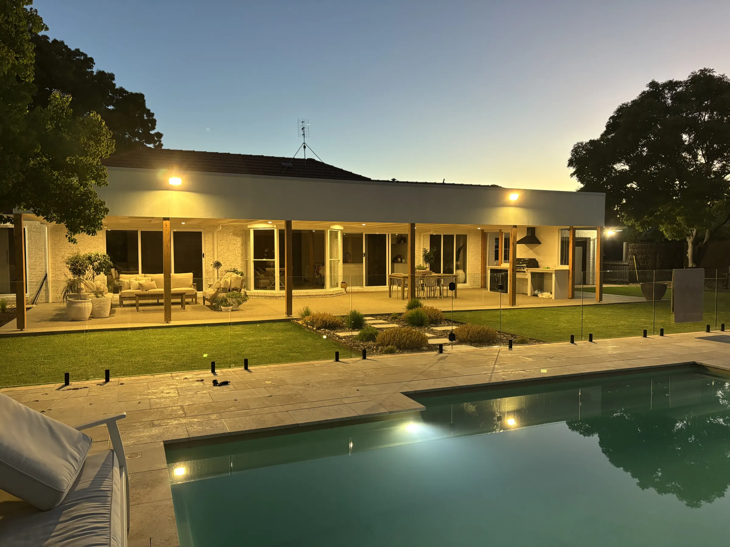 Single storey home at dusk with lit alfresco, eave lights and a pool in the foreground